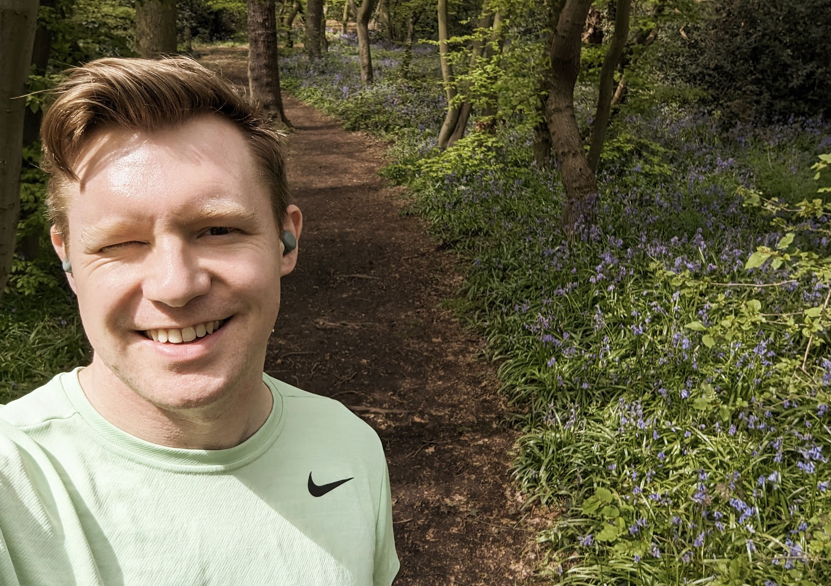 Photo of Tim Green smilling whilst on a run in Epping Forest, surrounded by bluebells and Hornbeam trees